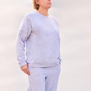 Può includere: Un completo composto da felpa e pantaloni della tuta grigio chiaro. La felpa girocollo ha maniche lunghe e orlo a coste. I pantaloni della tuta hanno vita con coulisse e tasche. L'outfit è realizzato in un materiale morbido e confortevole.