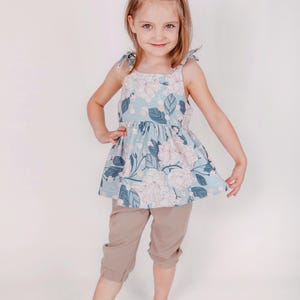 May include: A light blue floral print top with tie straps and matching tan capri pants. The top features a floral pattern in pink and blue, with a flared silhouette. The capri pants are a solid tan color, creating a coordinated outfit.
