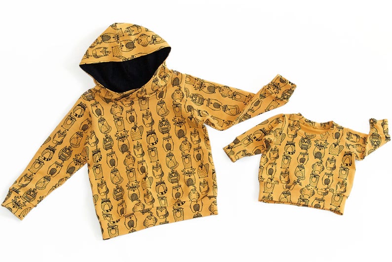 May include: Two mustard yellow hooded sweatshirts with a black and white animal print. The larger sweatshirt has a hood with a black lining.