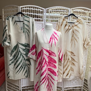 May include: Three linen dresses with a tropical leaf print. The dresses are in different colours: green, pink, and brown.