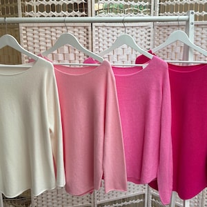May include: Four long-sleeved jumpers in various shades of pink, from white to fuchsia, hanging on hangers.