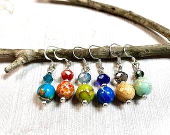 May include: Six pairs of dangle earrings with a silver hook and two beads. The top bead is a clear crystal and the bottom bead is a round, multi-colored stone. The stones are turquoise, orange, green, blue, beige, and light green.