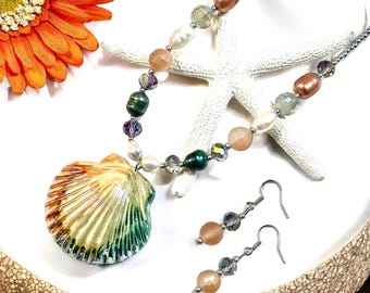 May include: A seashell pendant necklace and matching earrings. The necklace features a large, iridescent seashell pendant with a green, orange, and brown colour scheme. The necklace is made with a variety of beads, including white pearls, clear crystals, and green and peach-coloured beads. The earrings are simple silver hoops with a single peach-coloured bead and clear crystal.