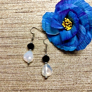 May include: A pair of silver dangle earrings with a white teardrop-shaped bead and a black bead on each earring.