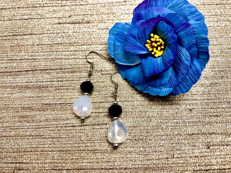 May include: A pair of silver dangle earrings with a white teardrop-shaped bead and a black bead on each earring.