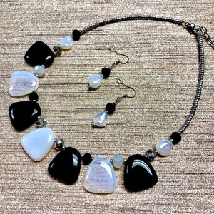 May include: A black and white necklace and earrings set with teardrop-shaped stones. The necklace has a silver chain and the earrings have silver hooks.