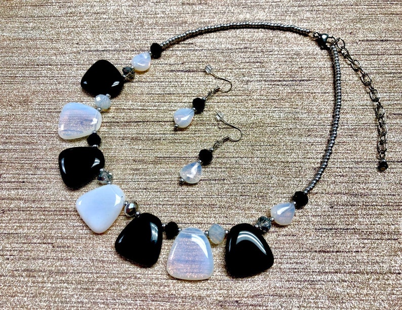 May include: A black and white necklace and earrings set with teardrop-shaped stones. The necklace has a silver chain and the earrings have silver hooks.