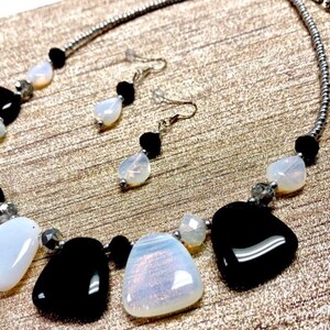 May include: A silver chain necklace with black and white gemstone beads. The necklace features a pendant with a large white gemstone and a smaller black gemstone. Matching earrings with a white gemstone and a black gemstone dangle from silver posts.