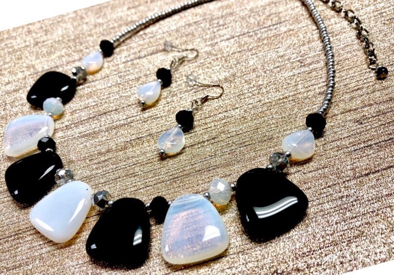 May include: A silver chain necklace with black and white gemstone beads. The necklace features a pendant with a large white gemstone and a smaller black gemstone. Matching earrings with a white gemstone and a black gemstone dangle from silver posts.