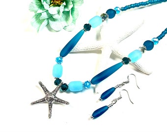 May include: A blue and turquoise glass bead necklace with a silver starfish pendant and matching earrings. The necklace features a variety of blue and turquoise beads, including round, oval, and long cylindrical beads.