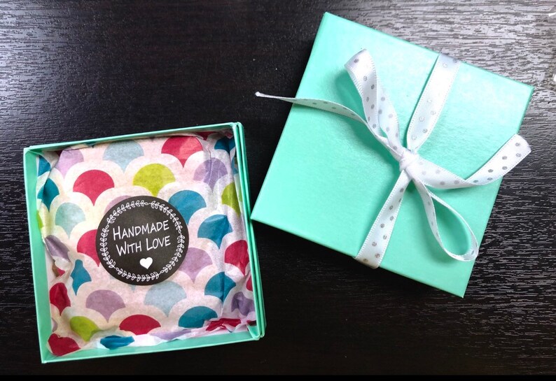 May include: A teal gift box with a white ribbon and white polka dots. The box is open and the inside is lined with colorful patterned tissue paper. A sticker on the tissue paper reads "Handmade with Love".