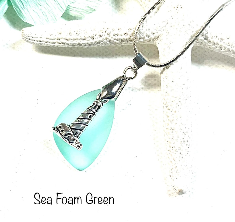 May include: A silver chain necklace with a light blue teardrop-shaped pendant featuring a silver lighthouse charm. The pendant is labeled "Sea Foam Green".