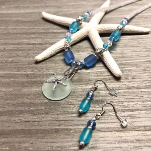 May include: A sea-themed necklace and earring set with a light blue glass pendant featuring a silver starfish charm. The necklace is made with light blue and silver beads and the earrings are made with light blue glass beads and silver hooks.