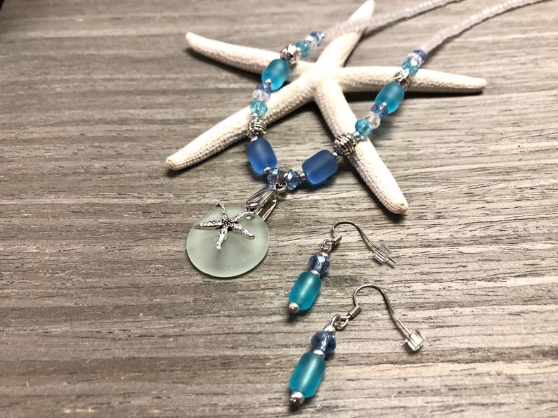 May include: A sea-themed necklace and earring set with a light blue glass pendant featuring a silver starfish charm. The necklace is made with light blue and silver beads and the earrings are made with light blue glass beads and silver hooks.