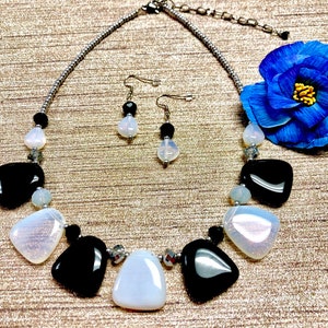 May include: A black and white necklace with a silver chain and matching earrings. The necklace features large, irregular shaped white and black stones. The earrings are simple silver posts with a single white stone.