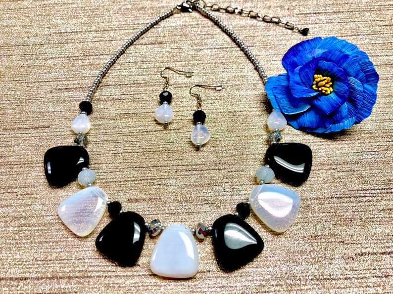 May include: A black and white necklace with a silver chain and matching earrings. The necklace features large, irregular shaped white and black stones. The earrings are simple silver posts with a single white stone.