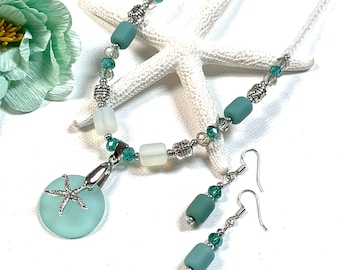 May include: A teal blue glass necklace and earrings set with a silver starfish pendant. The necklace features silver and clear beads, and the earrings have a single teal blue bead.