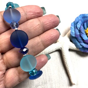 May include: A blue and turquoise glass bead bracelet with silver spacers. The beads are frosted and have a gradient of color.