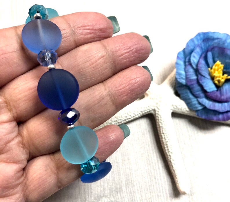 May include: A blue and turquoise glass bead bracelet with silver spacers. The beads are frosted and have a gradient of color.