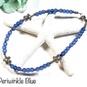 May include: A periwinkle blue beaded anklet with silver turtle charms. The anklet is on a white starfish background.