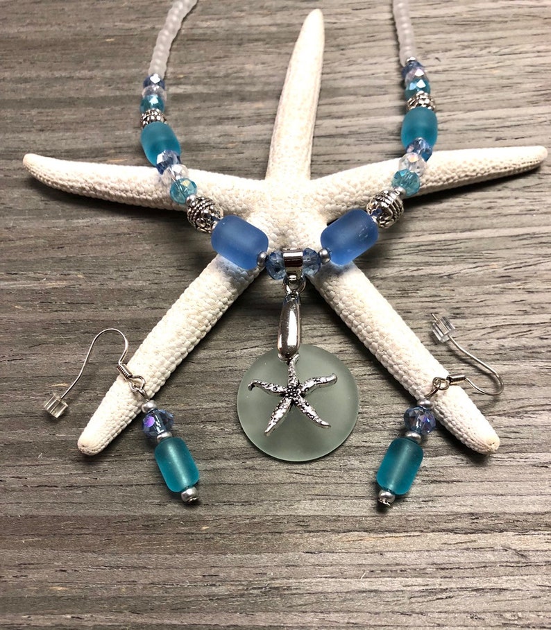 May include: A sea glass necklace and earrings set with a starfish pendant. The necklace features blue and clear glass beads with silver accents. The earrings are silver with blue glass beads.