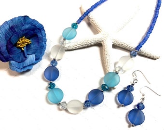 May include: A blue, white, and light blue glass bead necklace and matching earrings. The necklace is made with frosted glass beads and silver spacers. The earrings are made with frosted glass beads and silver hooks.