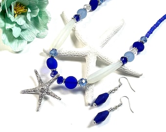 May include: A blue and white beaded necklace with a silver starfish pendant and matching blue and silver earrings. The necklace features frosted white beads, blue glass beads, and silver spacer beads.