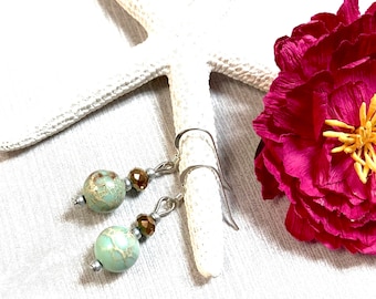 May include: A pair of silver dangle earrings with a light blue and brown marbled bead and a gold-toned crystal bead on each earring.