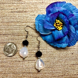 May include: A pair of dangle earrings with a white iridescent teardrop-shaped bead and a black bead on each earring.