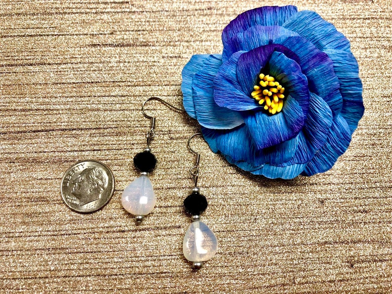 May include: A pair of dangle earrings with a white iridescent teardrop-shaped bead and a black bead on each earring.