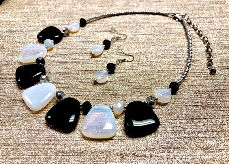 May include: A silver chain necklace with black and white teardrop-shaped beads. The necklace is paired with matching earrings.