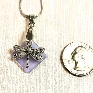 May include: A silver dragonfly pendant necklace with a lavender glass square charm. The charm is about the size of a US quarter.