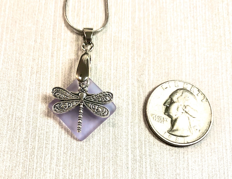 May include: A silver dragonfly pendant necklace with a lavender glass square charm. The charm is about the size of a US quarter.