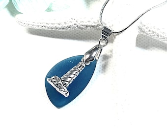 May include: A blue sea glass pendant necklace with a silver lighthouse charm. The necklace is on a silver chain.