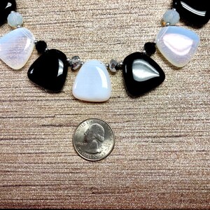May include: A close-up of a necklace with black and white triangular-shaped stones. The necklace is on a brown textured surface with a US quarter for scale.