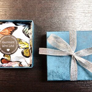 May include: A blue gift box with a silver ribbon and a white box with a butterfly pattern and a sticker that says "Handmade with Love".