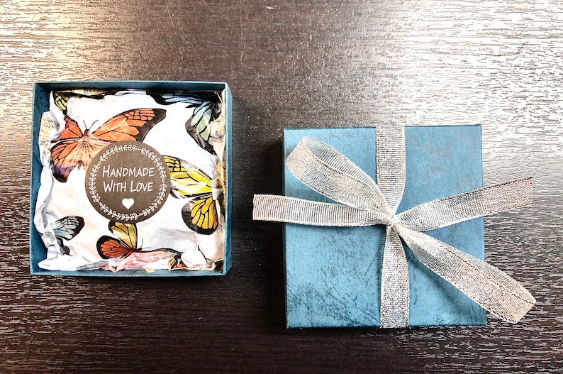 May include: A blue gift box with a silver ribbon and a white box with a butterfly pattern and a sticker that says "Handmade with Love".