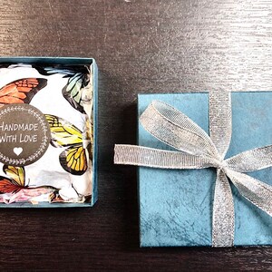 May include: A blue gift box with a silver ribbon and a white box with a butterfly pattern inside. The white box has a sticker that says "Handmade with Love".