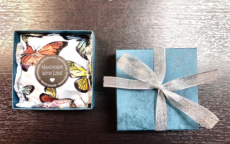 May include: A blue gift box with a silver ribbon and a white box with a butterfly pattern inside. The white box has a sticker that says "Handmade with Love".