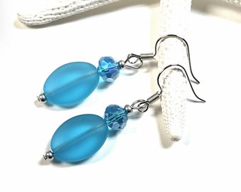 May include: A pair of dangle earrings with light blue oval glass beads and clear crystal accents. The earrings have silver hooks.