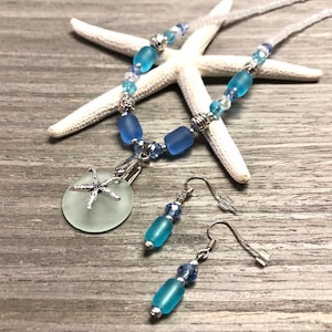May include: A sea glass necklace and earrings set with a starfish charm. The necklace features blue and clear glass beads with silver accents. The earrings are silver with blue glass beads.