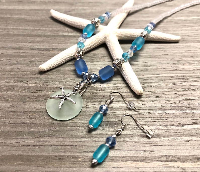 May include: A sea glass necklace and earrings set with a starfish charm. The necklace features blue and clear glass beads with silver accents. The earrings are silver with blue glass beads.