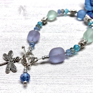 May include: A silver bracelet with blue and purple glass beads and a dragonfly charm. The bracelet has a toggle clasp.