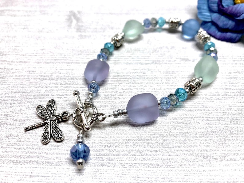May include: A silver bracelet with blue and purple glass beads and a dragonfly charm. The bracelet has a toggle clasp.