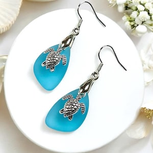 May include: Teal blue glass teardrop earrings with silver turtle charms. The earrings have silver hooks.