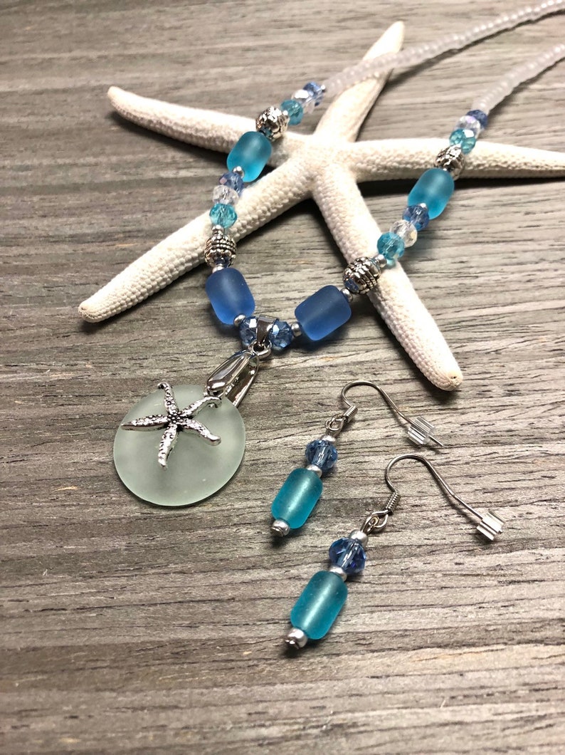 May include: A sea-themed jewelry set with a necklace and earrings. The necklace features a light blue glass pendant with a silver starfish charm. The earrings are silver with light blue glass beads.