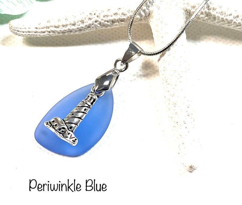 May include: A silver lighthouse charm pendant on a silver chain, hanging from a light blue sea glass teardrop.