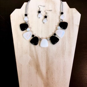 May include: A black and white statement necklace with matching earrings. The necklace features large, irregular shaped black and white beads.