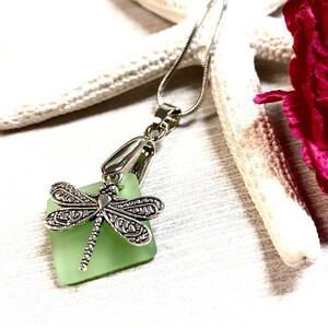 May include: A silver dragonfly charm pendant necklace with a light green square sea glass charm.