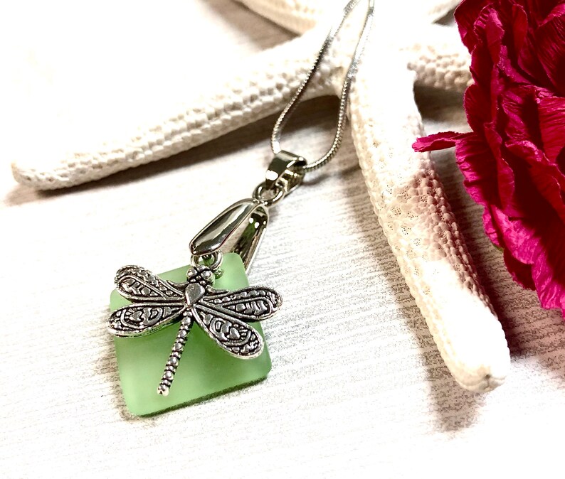 May include: A silver dragonfly charm pendant necklace with a light green square sea glass charm.